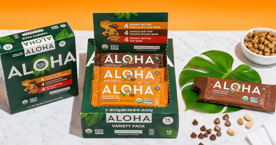 variety pack box of ALOHA Protein Bars on a table with a bite taken out of one bar
