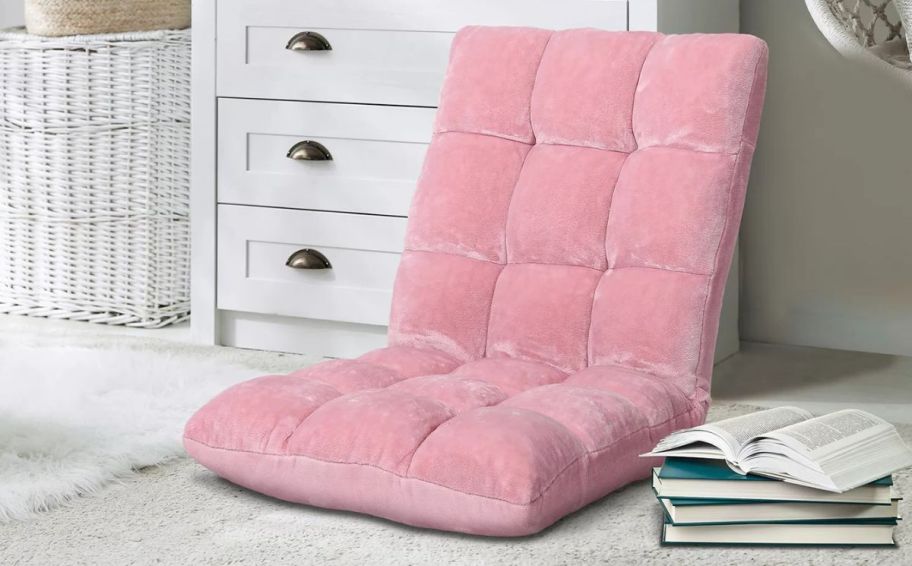 a pink velvet floor chair next to a stack of books