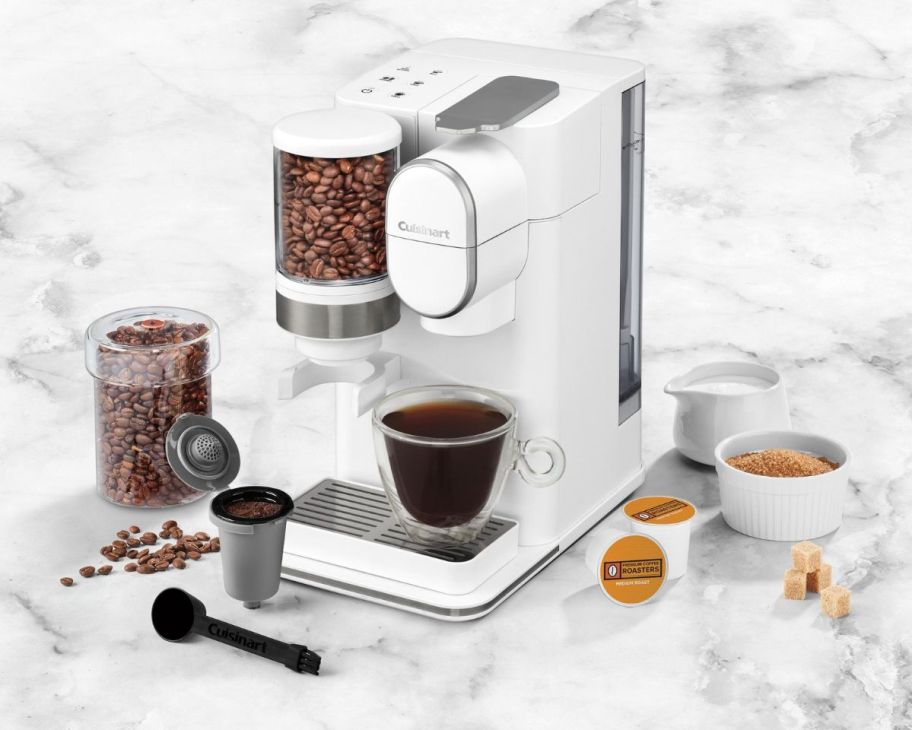 a white Cuisinart Grind Brew Single-Serve Coffee Maker shown with accessories, and k-cups on a white marble counter