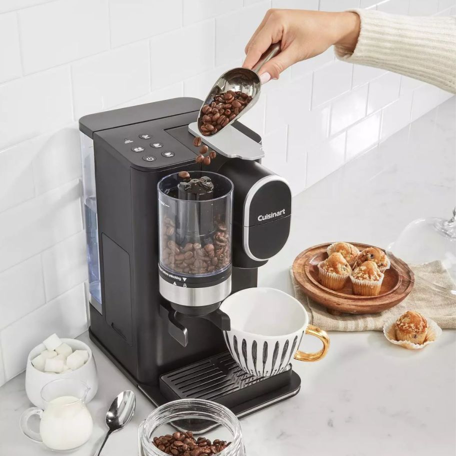 a black Cuisinart Grind Brew Single-Serve Coffee Maker shown with accessories, and k-cups on a white marble counter
