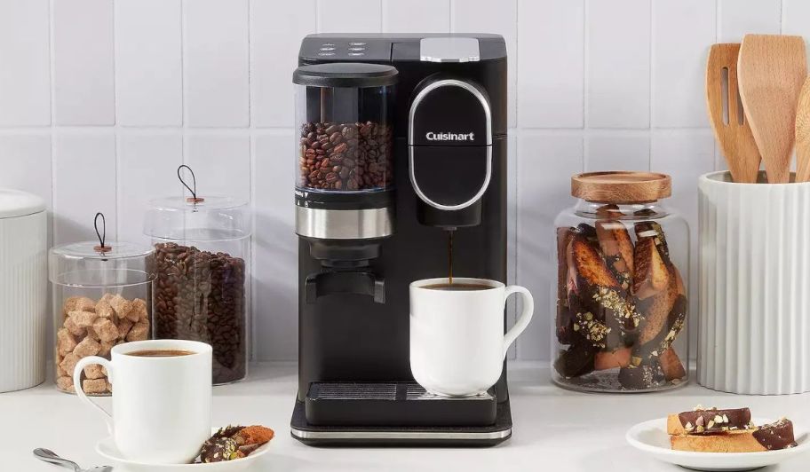 a black Cuisinart Grind Brew Single-Serve Coffee Maker shown with accessories, and k-cups on a white marble counter