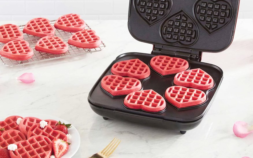 6 pink waffles on waffle maker near rack of cooling waffles