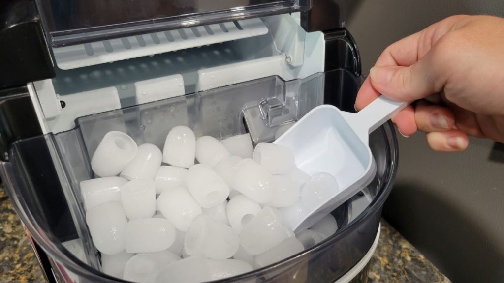 Hand holding a scoop in an ice machine to scoop out ice