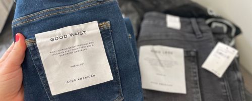 Hand holding a pair of Good American jeans next to another pair