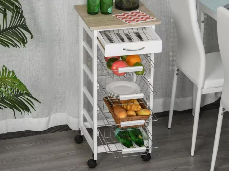 white wooden kitchen storage cart with wire basket pull outs sitting in a kitchen by a table and chairs