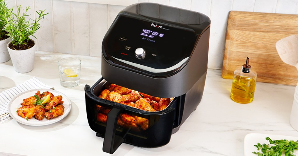 black air fryer with viewing window on kitchen counter next to plate of wings
