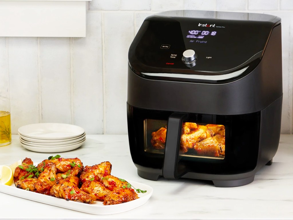 black air fryer with viewing window on kitchen counter next to plate of wings