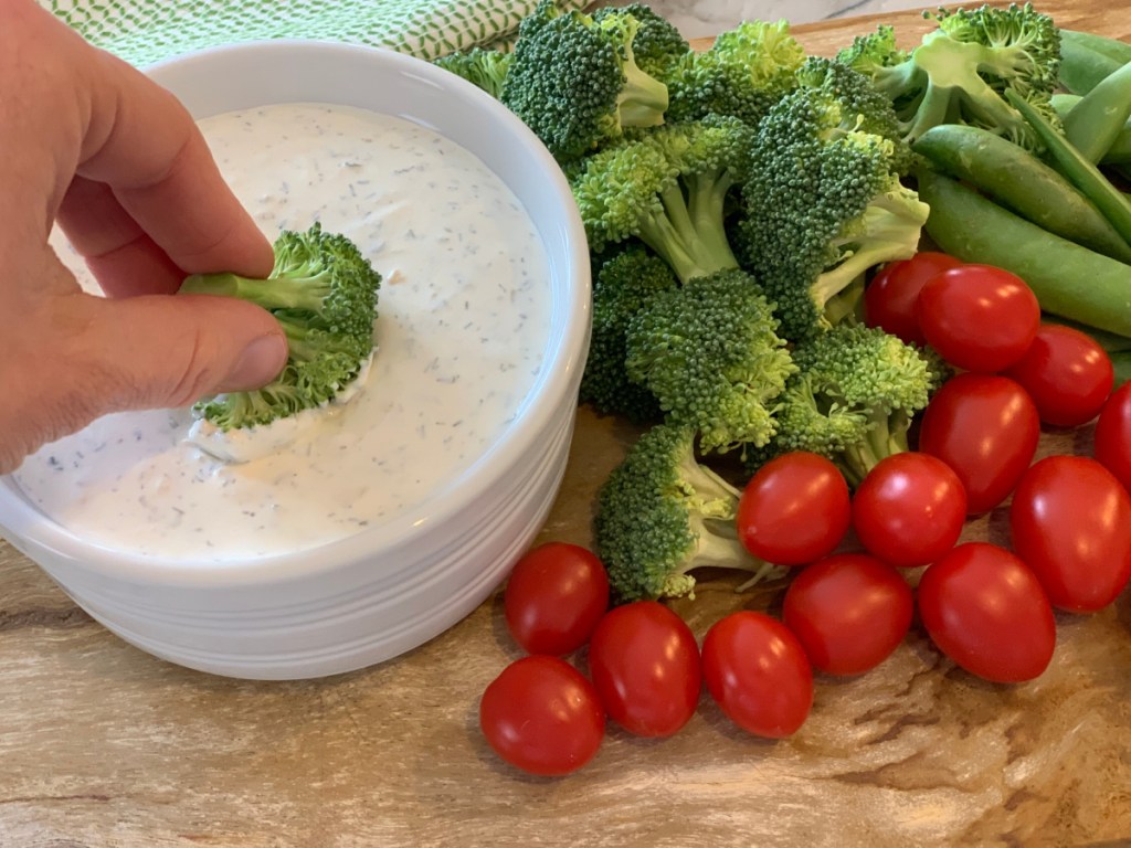 hand dipping a broccoli floret into low carb keto ranch dip