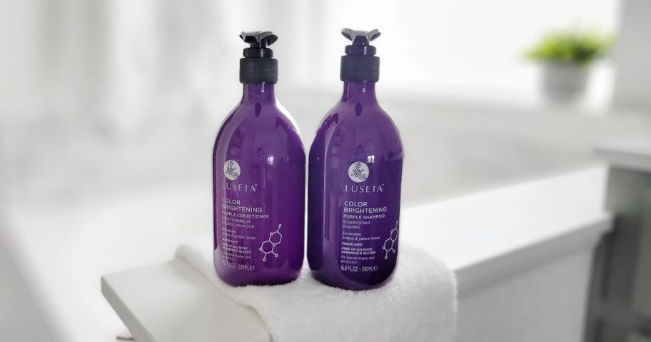 purple shampoo and conditioner bottles on a towel in a bathroom