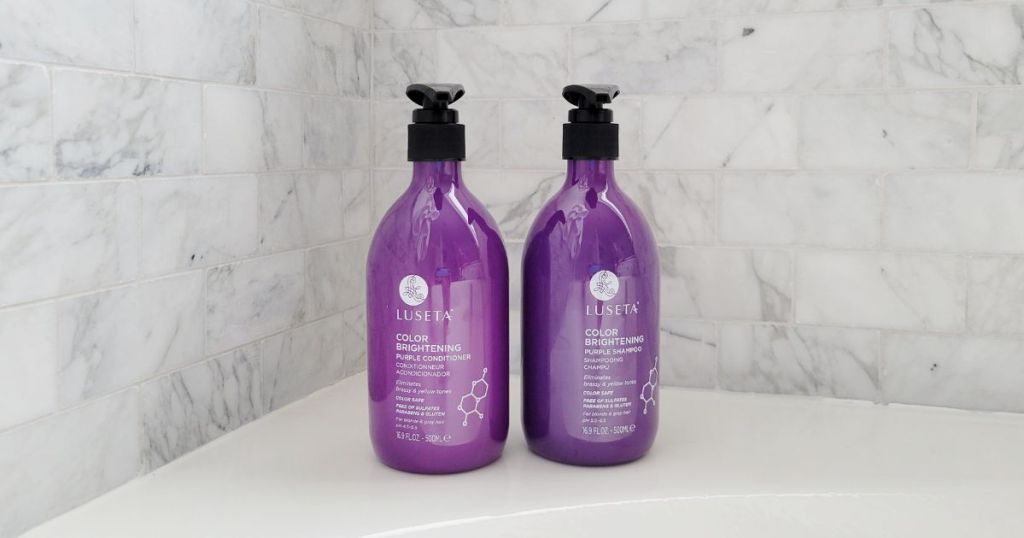 Luseta Purple Shampoo and Conditioner bottles on corner of tub with marble tile