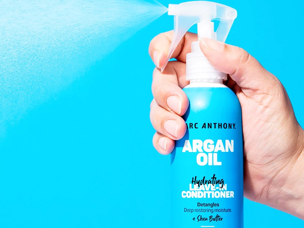 hand spraying a blue bottle of Marc Anthony Argan Oil Leave-In Conditioner Spray