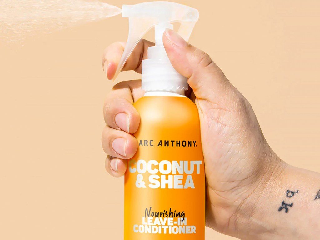 hand spraying an orange bottle of Marc Anthony Coconut & Shea Leave-In Conditioner Spray