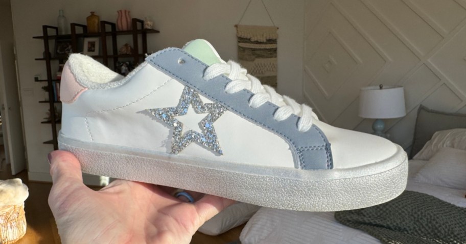 hand holding up a women's white sneaker with a silver star