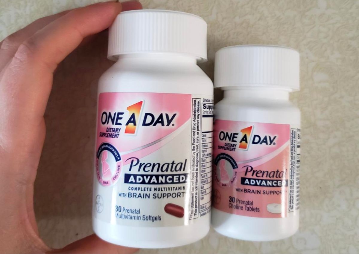 a womans hand displaying a bottle of One A Day Womens’ Prenatal Advanced Complete Multivitamin next to a bottle of choline