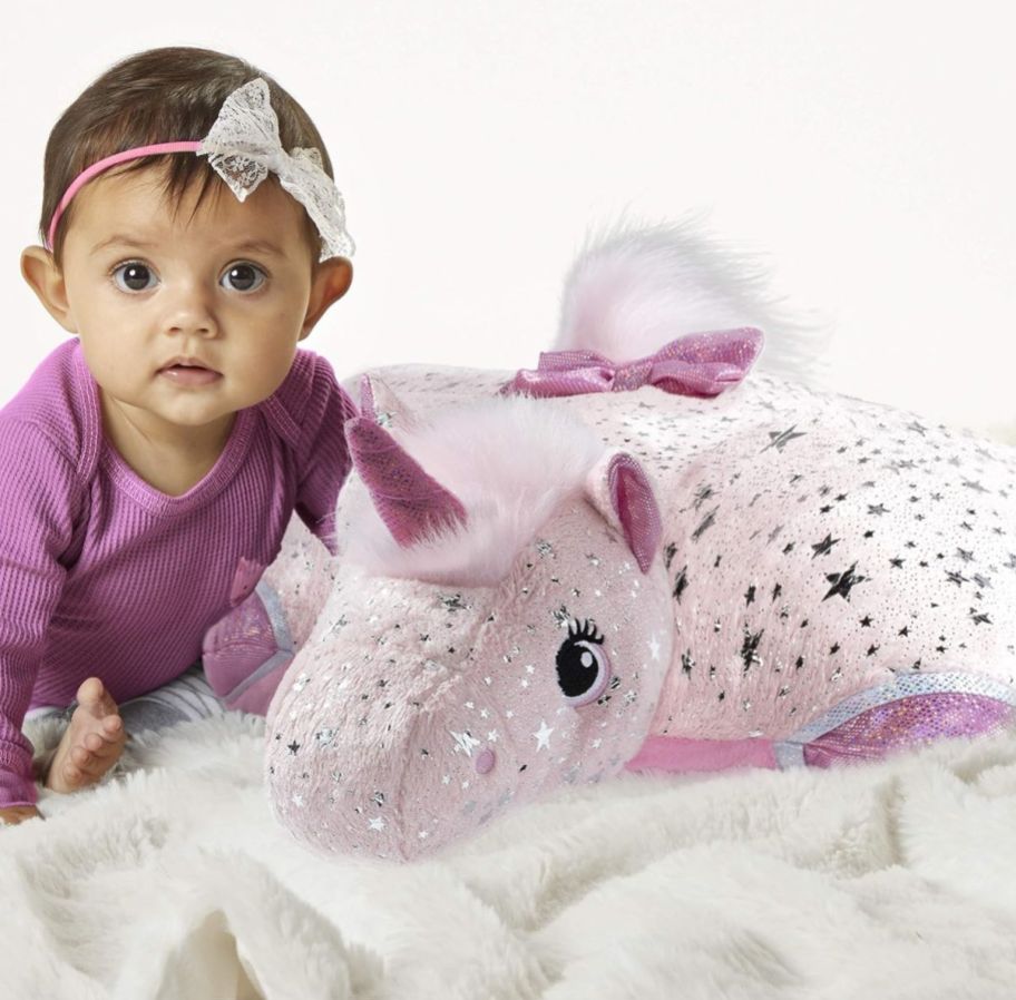 a little baby girl with a pink unicorn pillow pet