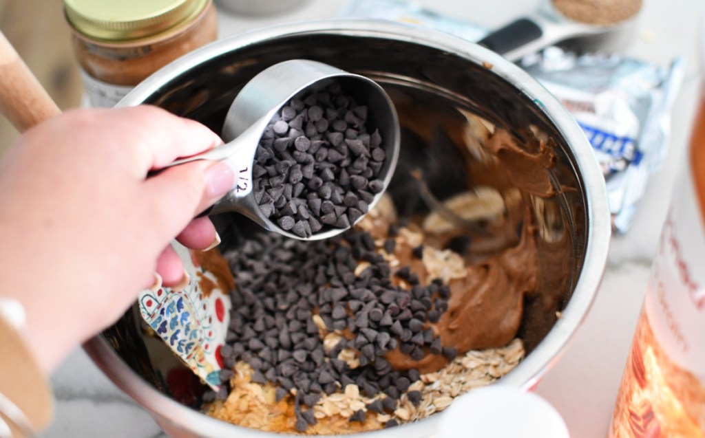 Pouring a measuring cup of chocolate chips into a mixing bowl with other ingredients for oatmeal energy bites