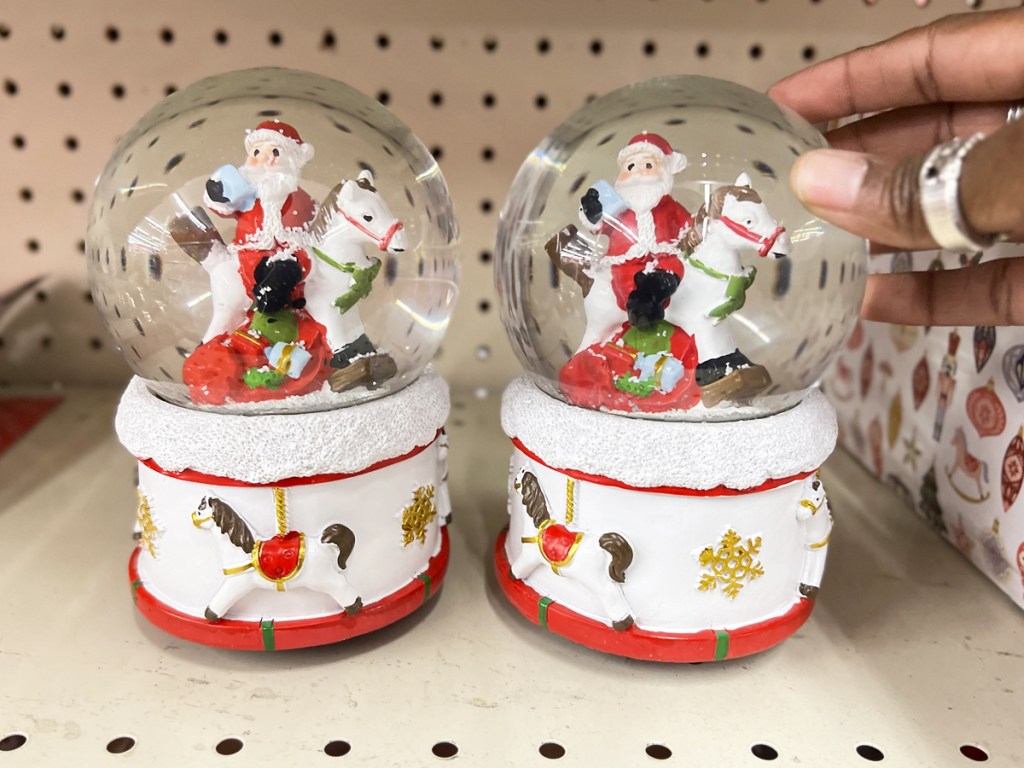 hand touching santa snow globes on store shelf