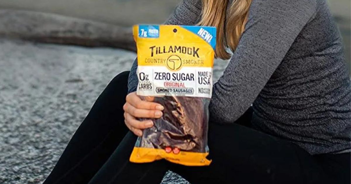 A woman holding a bag of tillamook smoked sausage snacks sitting by a mountain lake