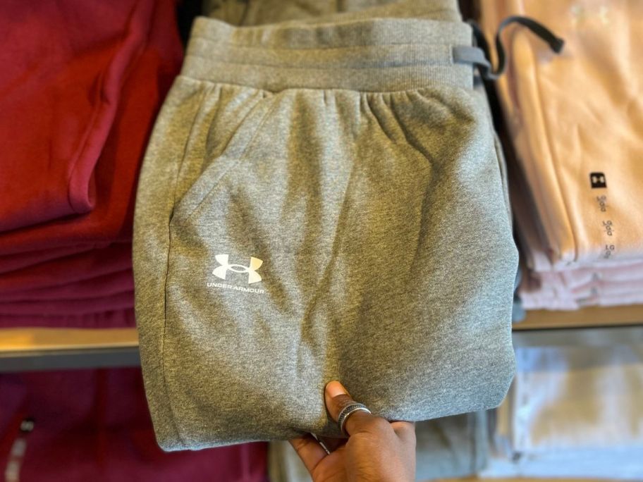 a hand holding a folded pair of Under Armour gray women's sweatpants
