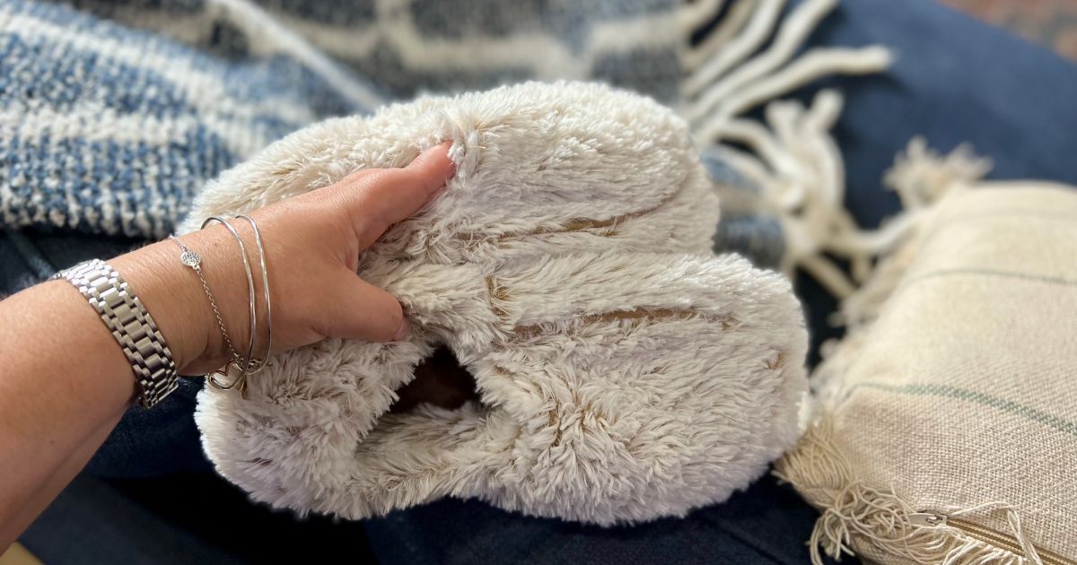 A woman's hand holding a pair of Warmies slippers