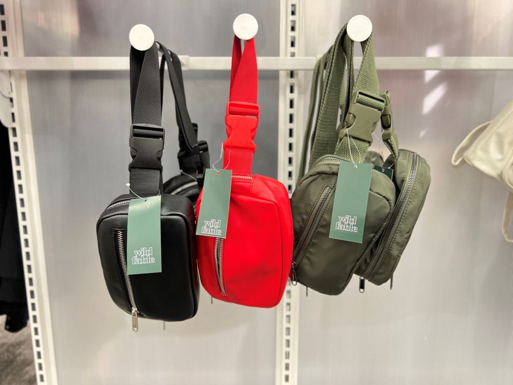 One black, one red, and one green belt bag hanging on hooks at Target