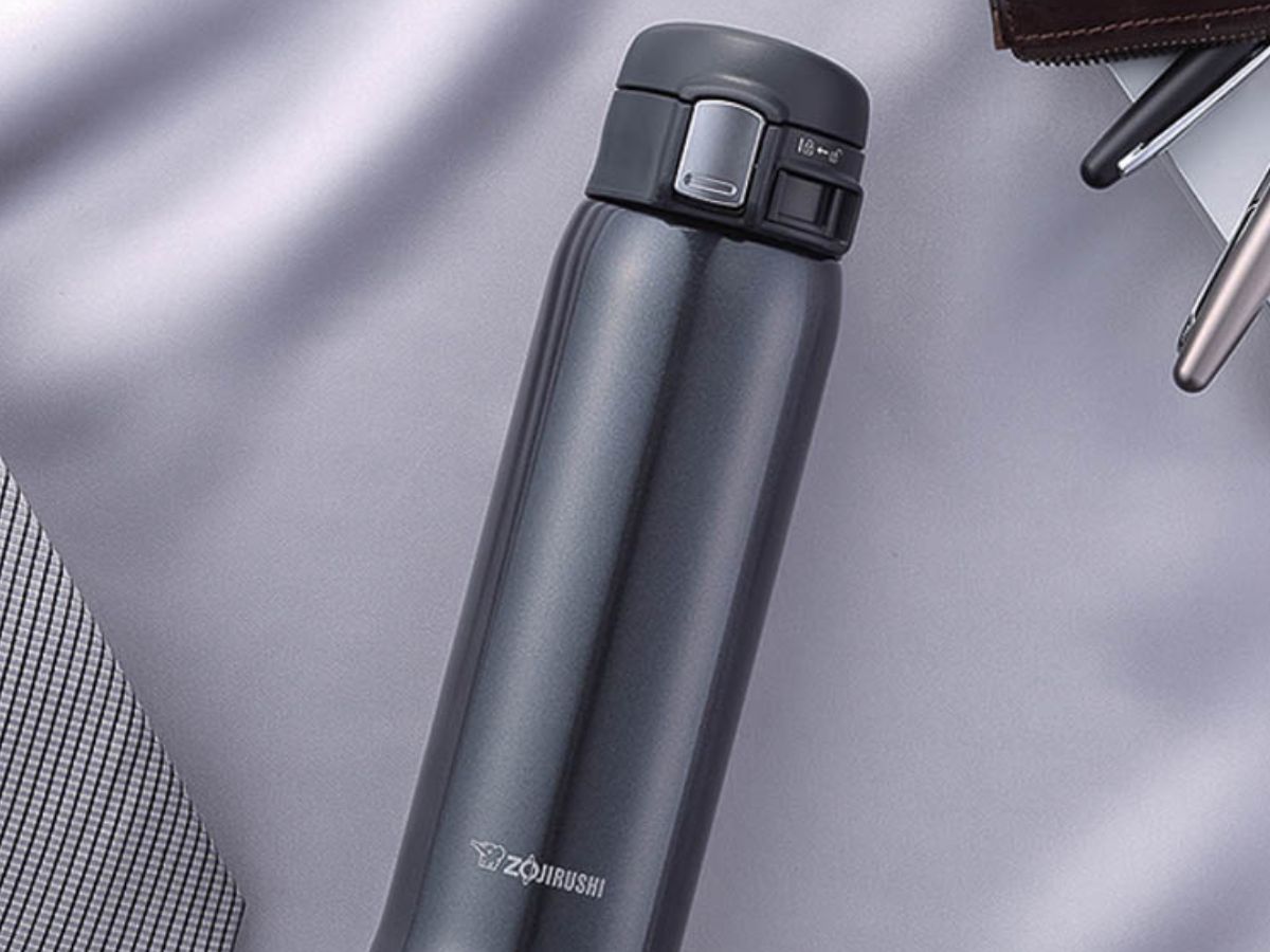 black travel mug laying on a shirt with pens next to it