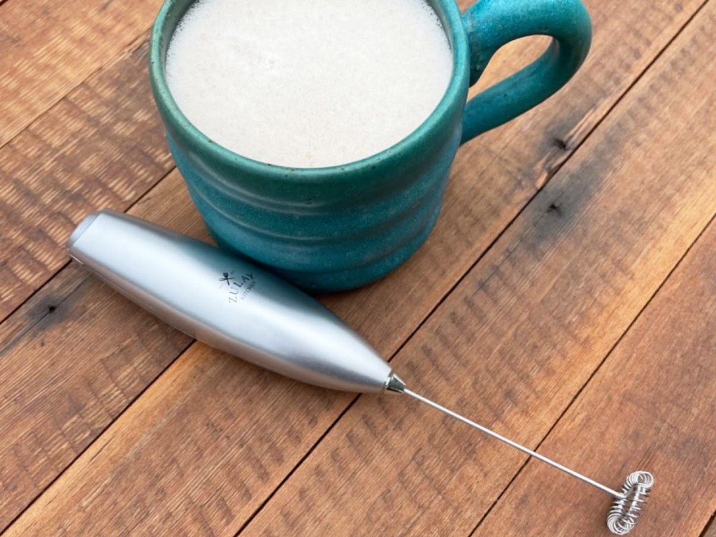 silver milk frother next to cup of coffee