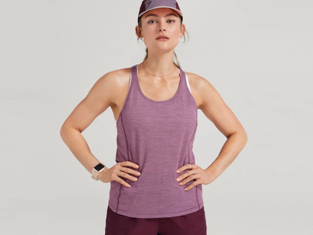 woman wearing a hat and allbirds top looking at the camera with her hands on her hips