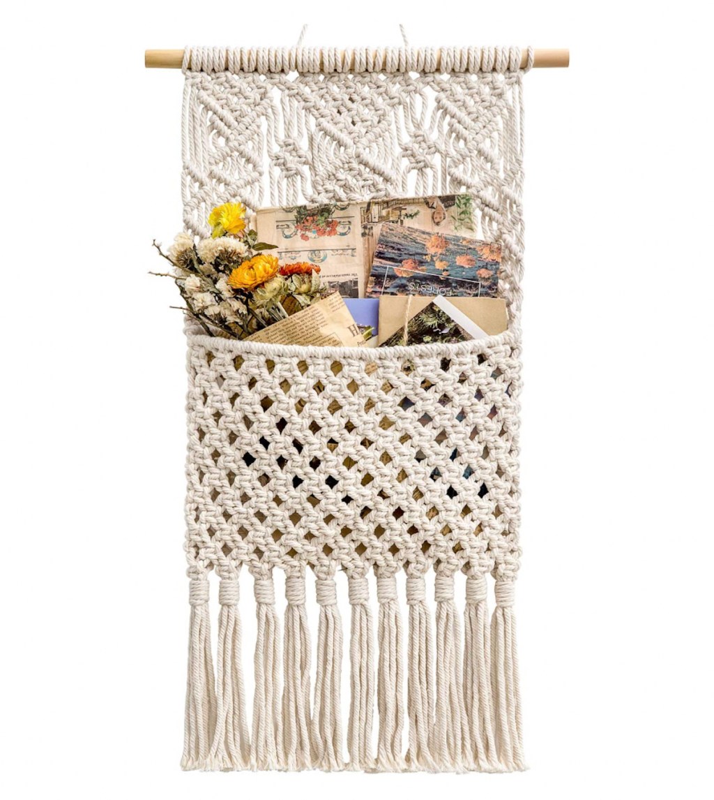macrame mail sorter with flowers and postcards inside on white background 