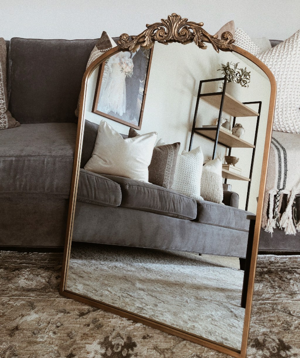 gold mirror on rug leaning on gray couch 