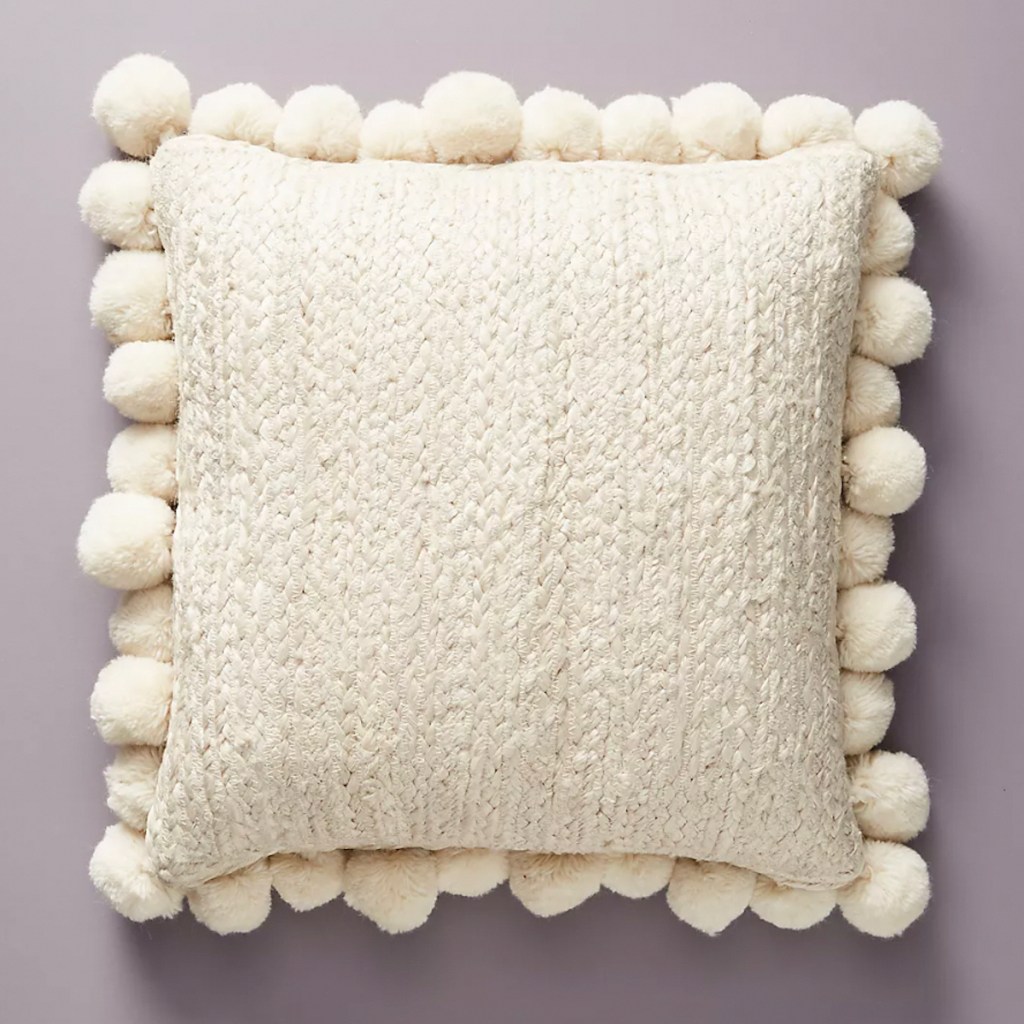 cream pom throw pillow on purple background 