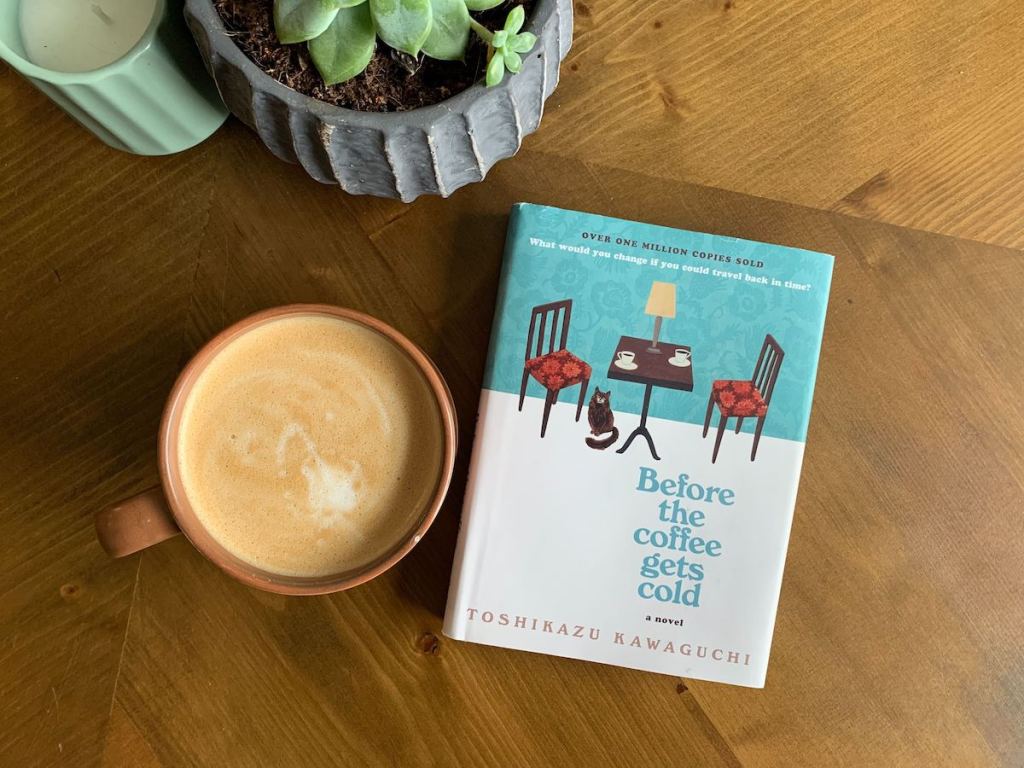 before the coffee gets cold book sitting on wood table next to coffee and plant 