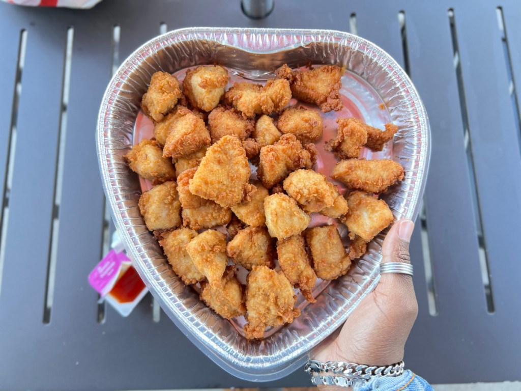 hand lifting up a heart shaped tray of chick fil a chicken nuggets