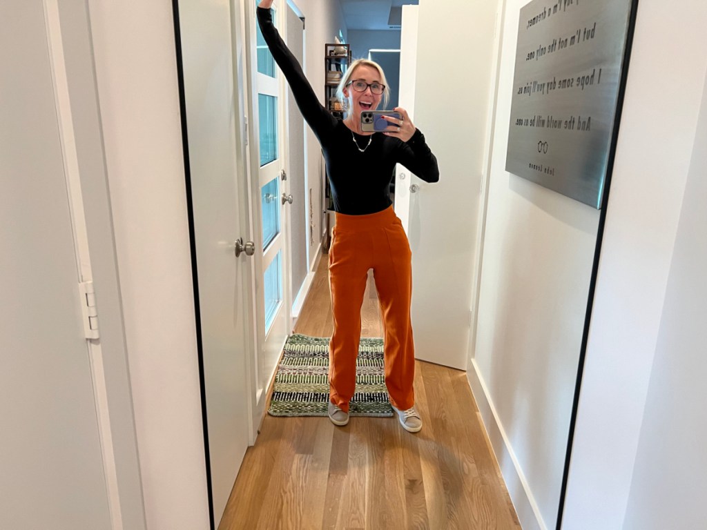 woman wearing orange athleta pants taking a picture in front of a full length mirror