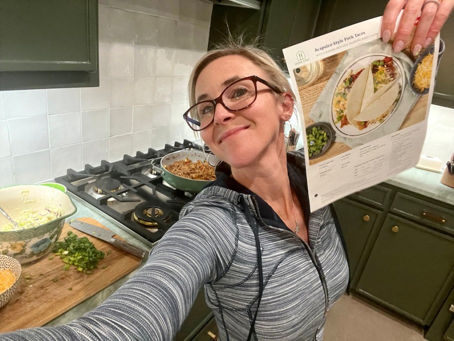 woman holding up Home Chef recipe in kitchen