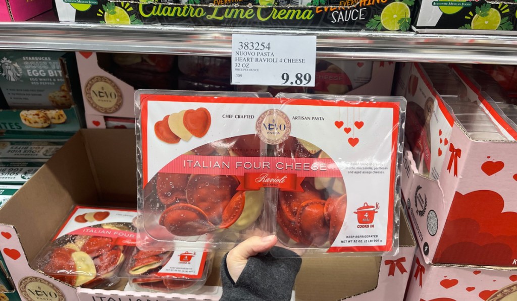 woman holding up a package of costco heart-shaped ravioli in front of a price sign