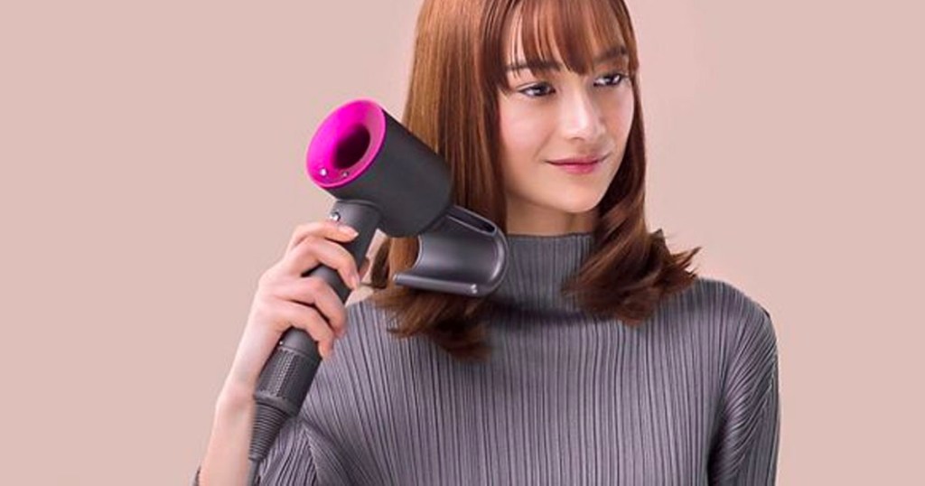 woman in gray turtleneck shirt using gray and pink dyson hair dryer