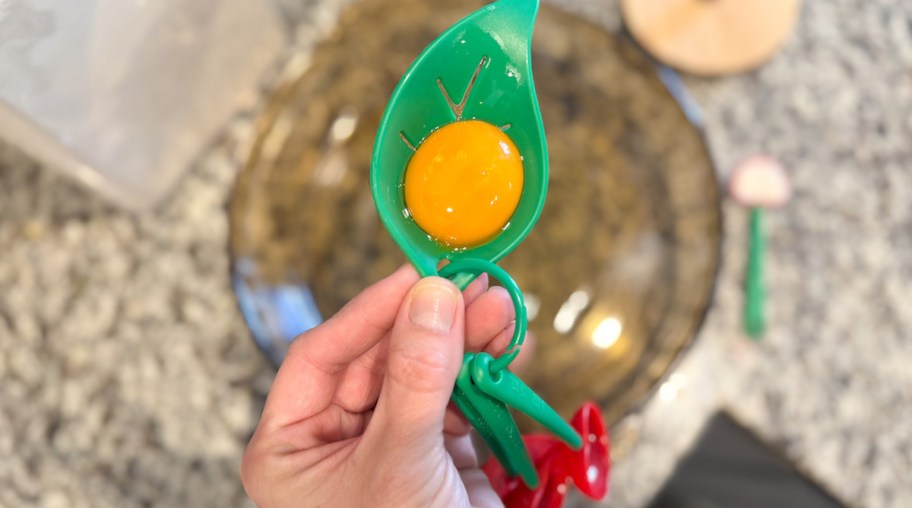 egg yolk holding green measuring cup over glass bowl