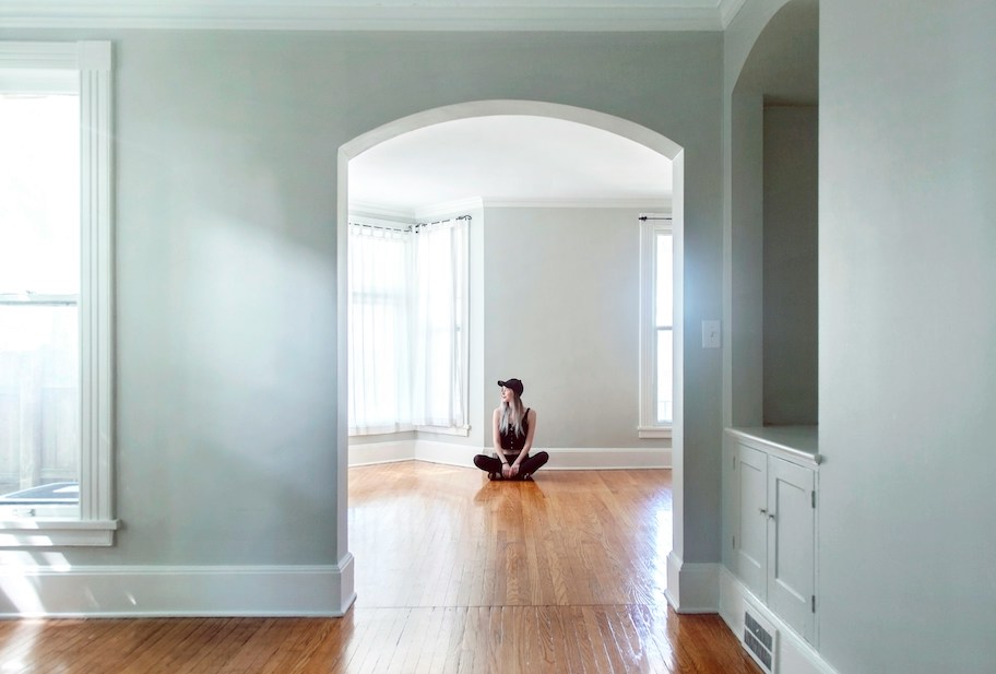 woman sitting in the middle of a wooden floor in empty house with windows