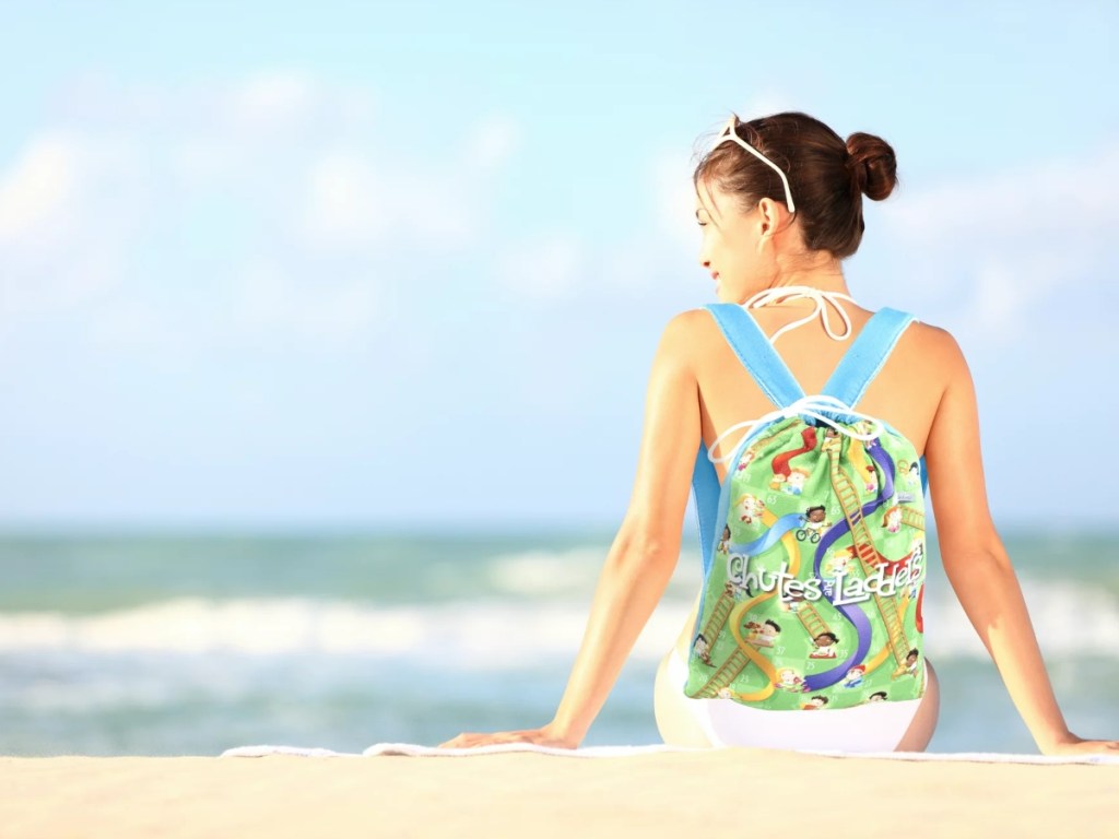 woman on beach wearing Chutes & Ladders backpack