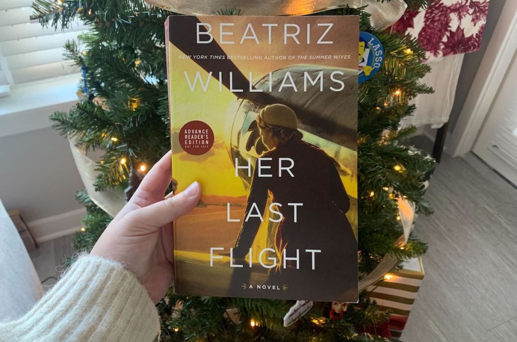 hand holding her last flight book in front of lit christmas tree 