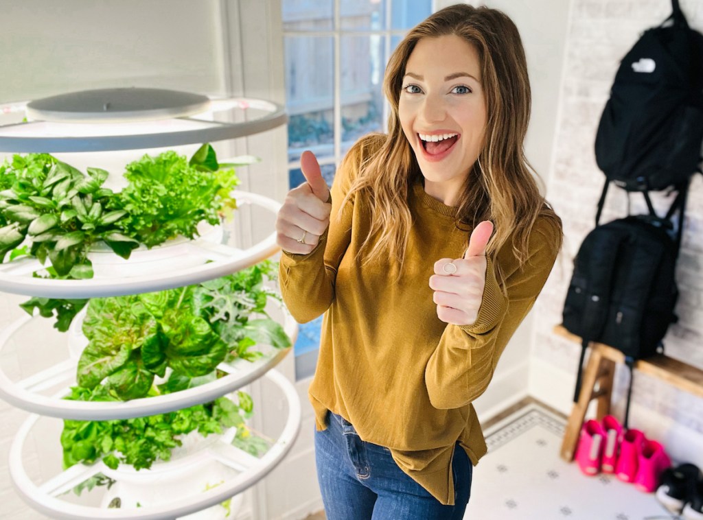 woman giving two thumbs up standing next to hydroponic garden