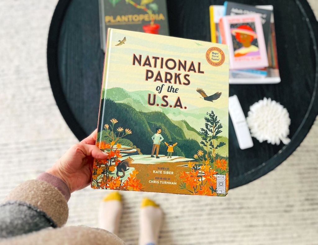 hand holding the national parks of the usa book over coffee table 