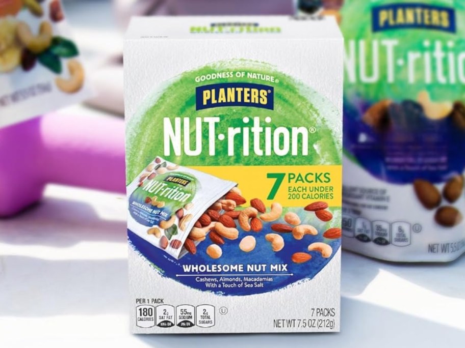 box of Planters NUT-rition Wholesome Nut Mix on a table with pouches behind it
