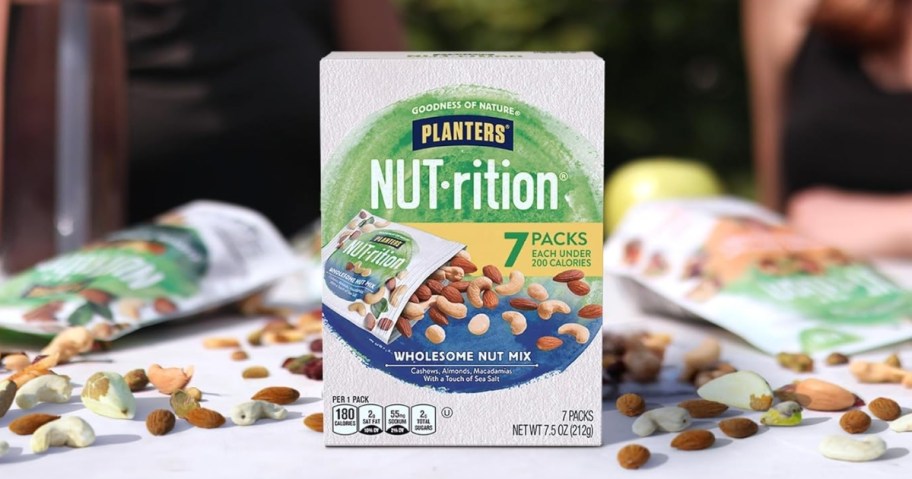 box of Planters NUT-rition Wholesome Nut Mix on a table with pouches open and nuts spilling out behind it