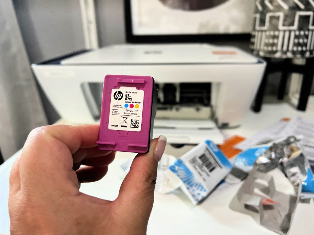 A woman is holding a color refill for a HP printer in her office.