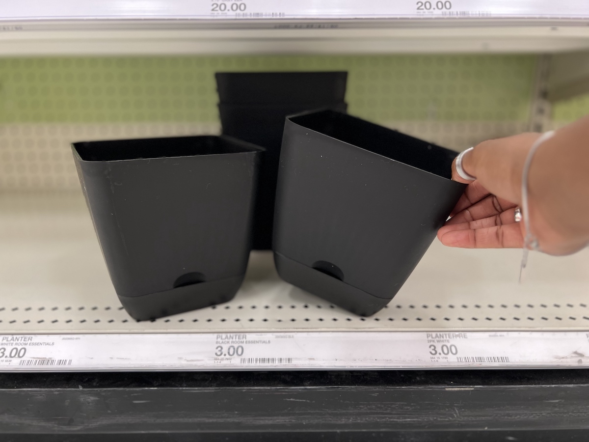 hand grabbing one black self watering planters on store shelf
