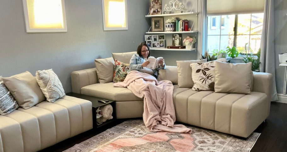 woman sitting on cream colored sectional couch reading a book