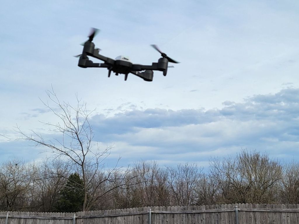 Aatop Drone flying in sky with fence and trees in the background