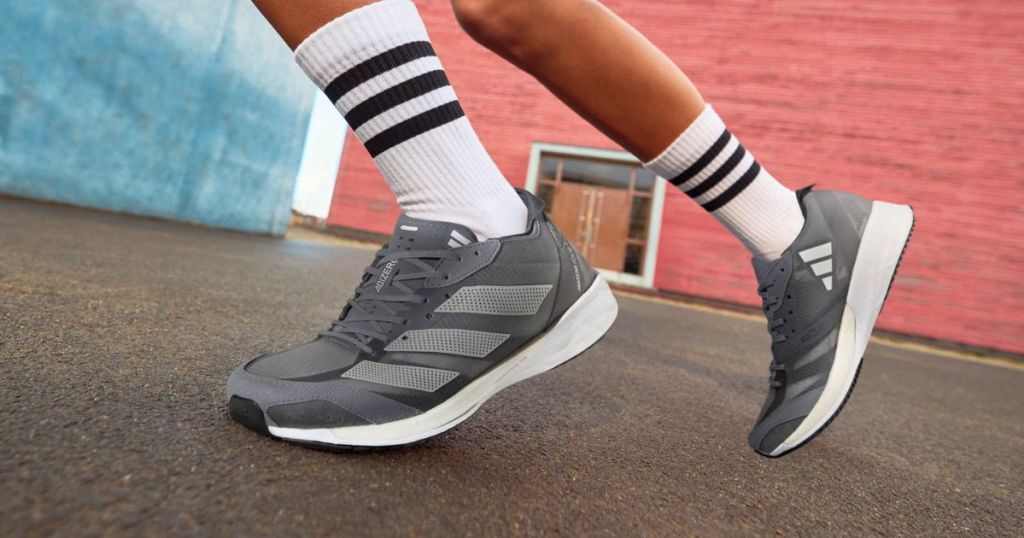 Person wearing grey and white adidas running shoes with tall white and black socks